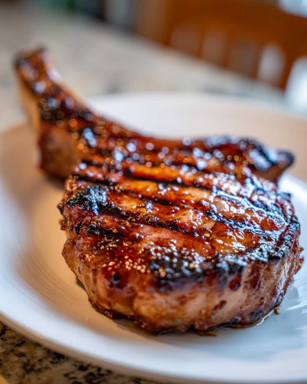 Close-up of a thick, glazed, grilled pork chop showing distinct grill marks, likely after using a marinade for pork chops.