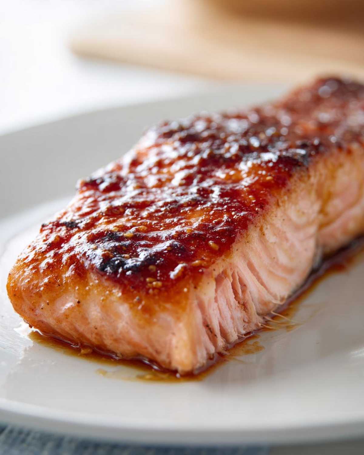 Close-up of a perfectly cooked, glazed salmon fillet resting on a white plate, showing moist texture.