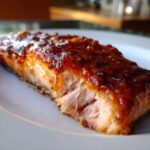 Close-up of a perfectly cooked, flaky salmon fillet topped with a thick, shiny, dark glaze.