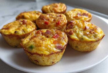 A close-up of six freshly baked Egg Muffin Cups with visible bits of bacon and peppers, served on a white plate.