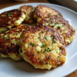 Close-up of several perfectly pan-fried mashed potato cakes garnished with fresh green chives on a white plate.