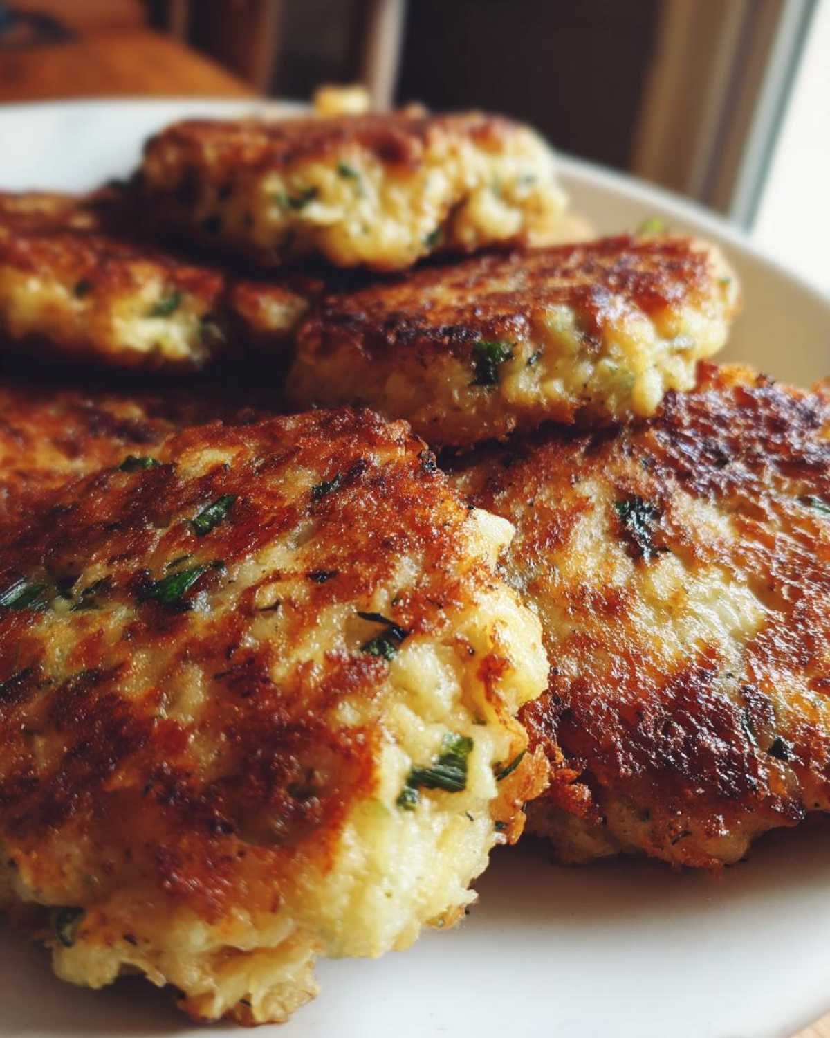 Close-up of several golden brown, pan-fried mashed potato cakes flecked with green herbs.