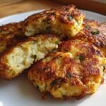 A close-up of several golden brown, pan-fried mashed potato cakes, one cut open to show the fluffy interior.