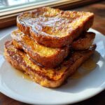 A tall stack of golden brown easy french toast slices drizzled generously with syrup and dusted with powdered sugar.