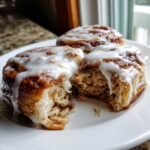 Three freshly baked cinnamon rolls covered in thick white icing, one is broken open to show the soft interior.