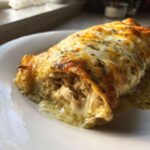 Close-up of a single green chile chicken enchiladas, oozing with melted cheese and green sauce.