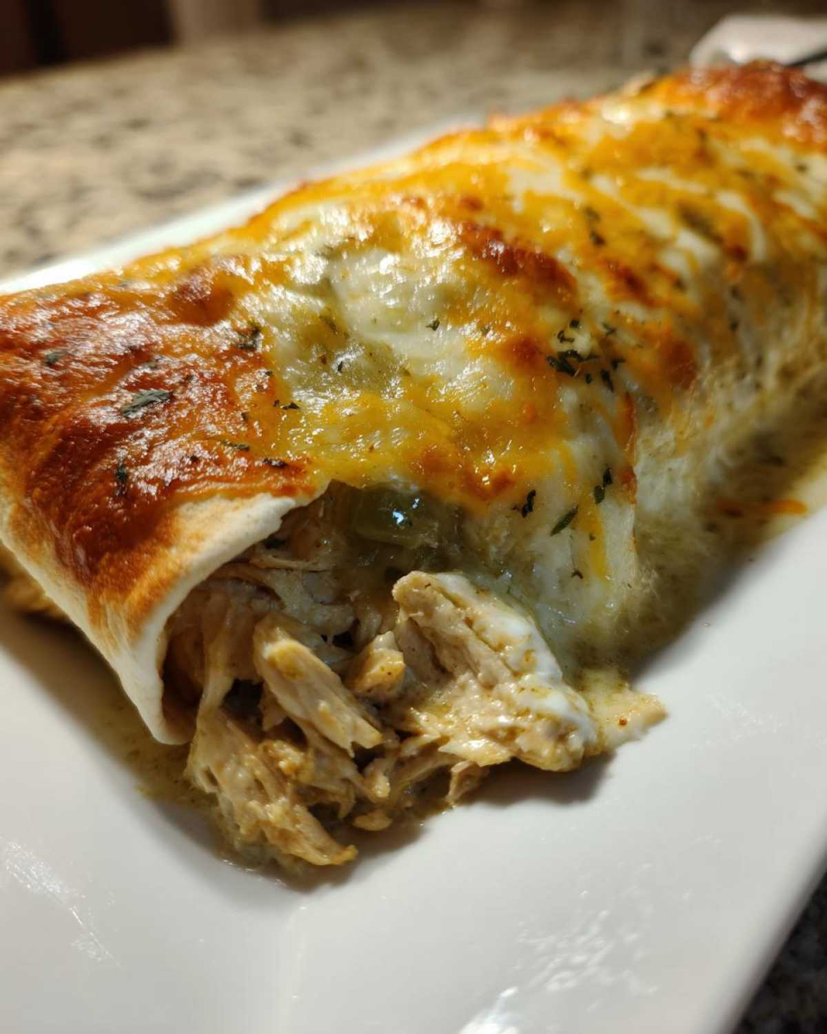Close-up of a green chile chicken enchiladas showing shredded chicken filling spilling out from under melted cheese.