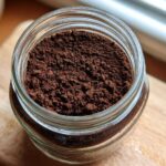 Close-up overhead view of rich, dark brown homemade hot cocoa mix powder stored in a clear glass jar.