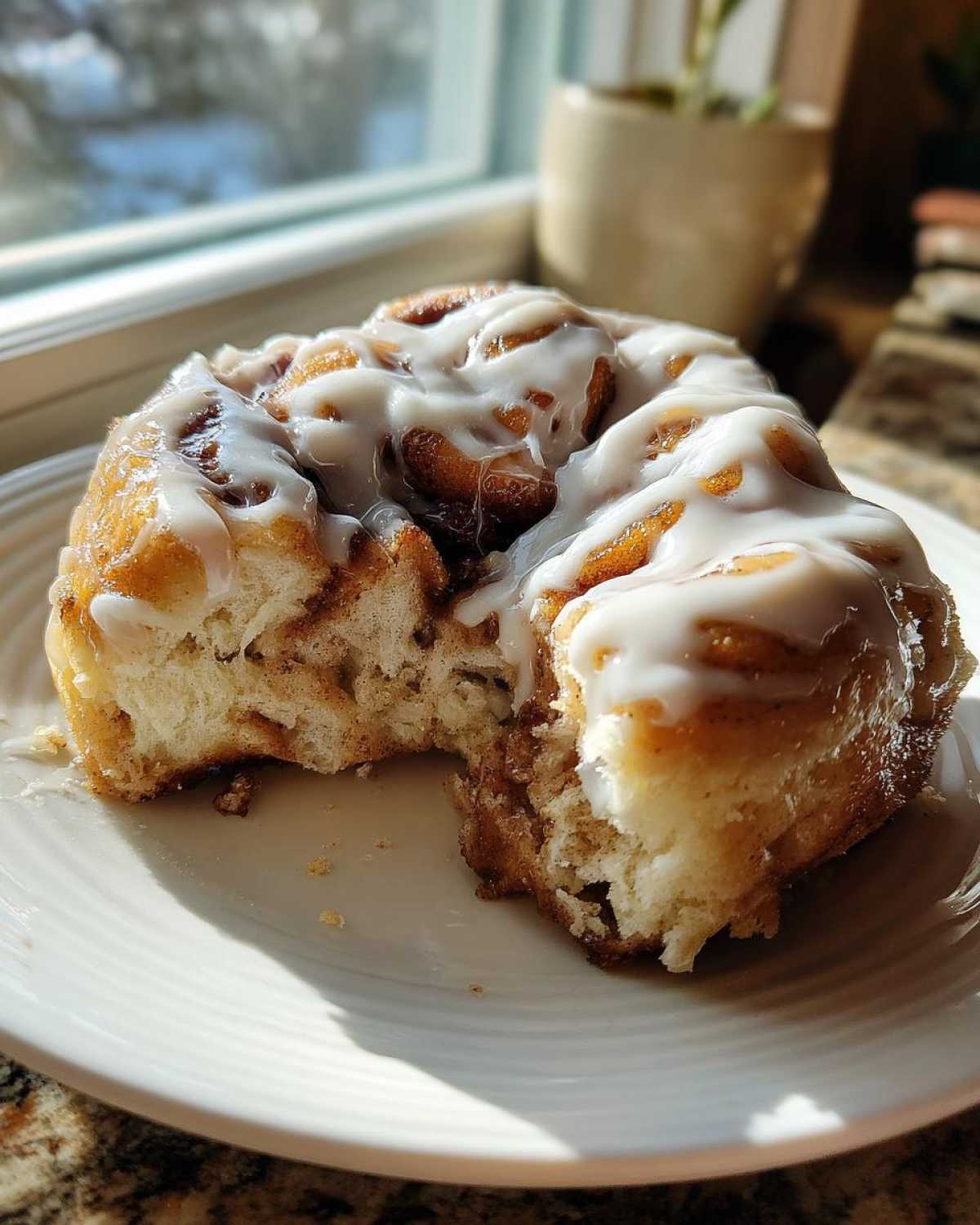 A soft, gooey cinnamon roll covered in white icing, with a piece broken off to show the fluffy interior.