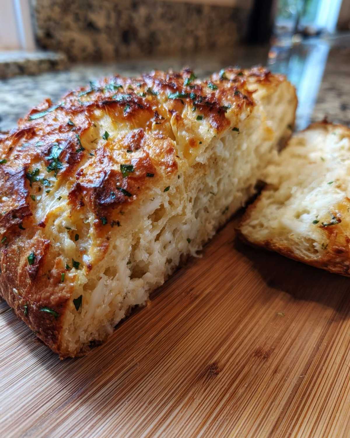 Close-up of freshly baked Italian herb and cheese bread, showing a golden, cheesy top sprinkled with parsley.