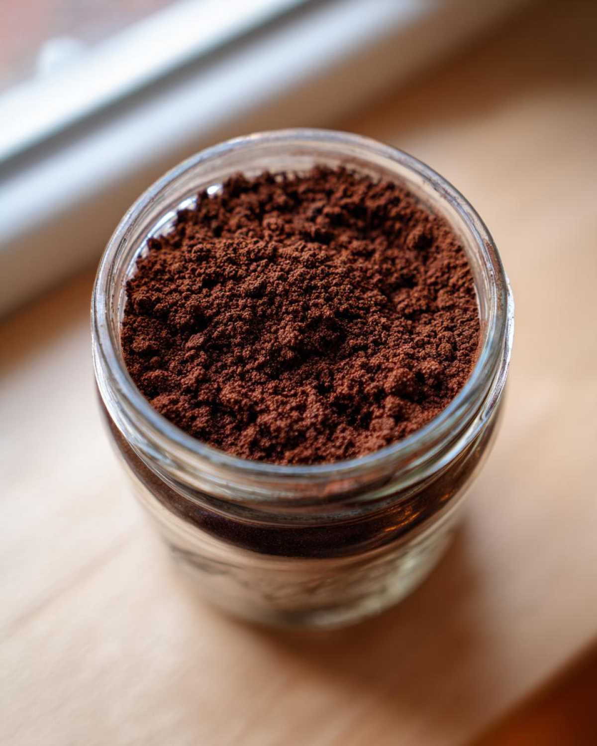 A close-up view of rich, dark brown homemade hot cocoa mix filling a small glass jar.
