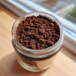 Close-up of rich, dark brown hot cocoa mix powder filling a clear glass jar.