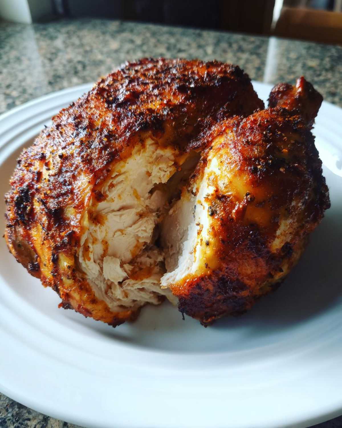 A whole chicken cooked in the air fryer, cut open to show juicy white meat and crispy seasoned skin.