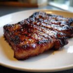 Close-up of a perfectly cooked, juicy pork steak recipe with a dark, caramelized glaze on a white plate.