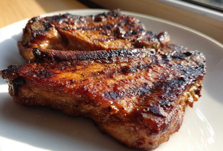 Two perfectly grilled and glazed pork steak cuts resting on a white plate, showing caramelized char marks.