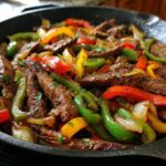 Close-up of sizzling steak fajitas with colorful bell peppers and onions in a cast iron skillet.