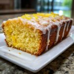 A close-up of a moist slice of lemon pound cake drizzled with white glaze and topped with lemon zest.