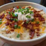 A creamy bowl of loaded baked potato soup topped with bacon, cheddar cheese, sour cream, and chives.