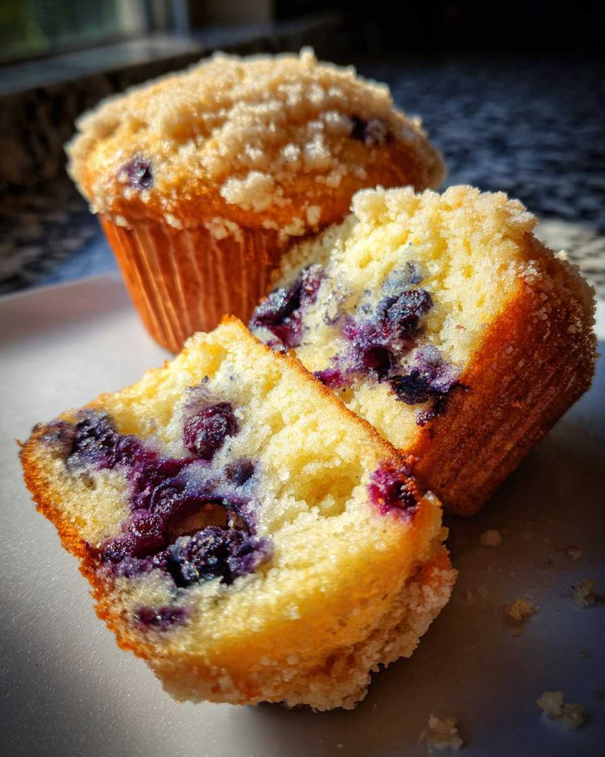 Close-up of a blueberry muffin cut in half showing the moist interior packed with blueberries, topped with a sugary crumb.