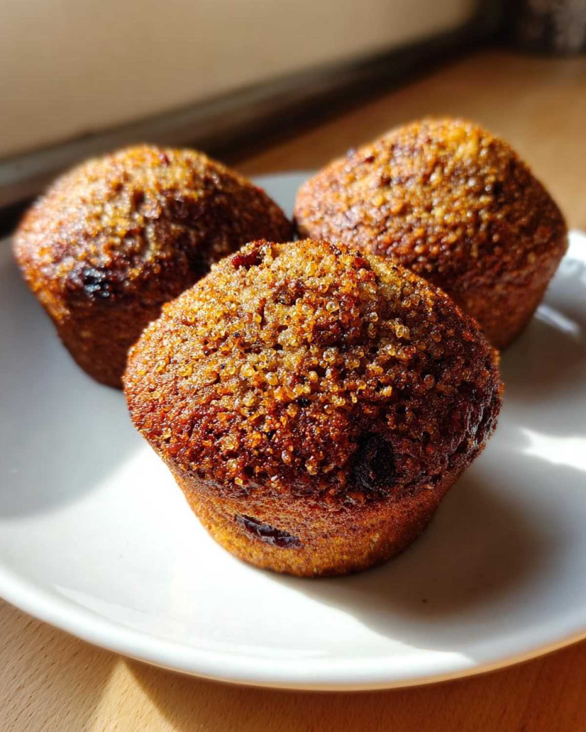 Three freshly baked, moist bran muffins with a coarse, sugary topping, resting on a white plate.