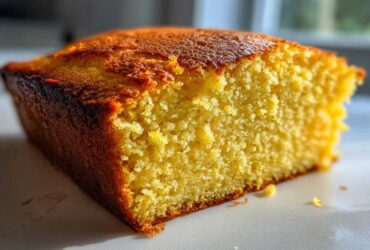 Close-up of a thick, moist slice of golden buttermilk cornbread showing its crumb texture and dark, baked crust.