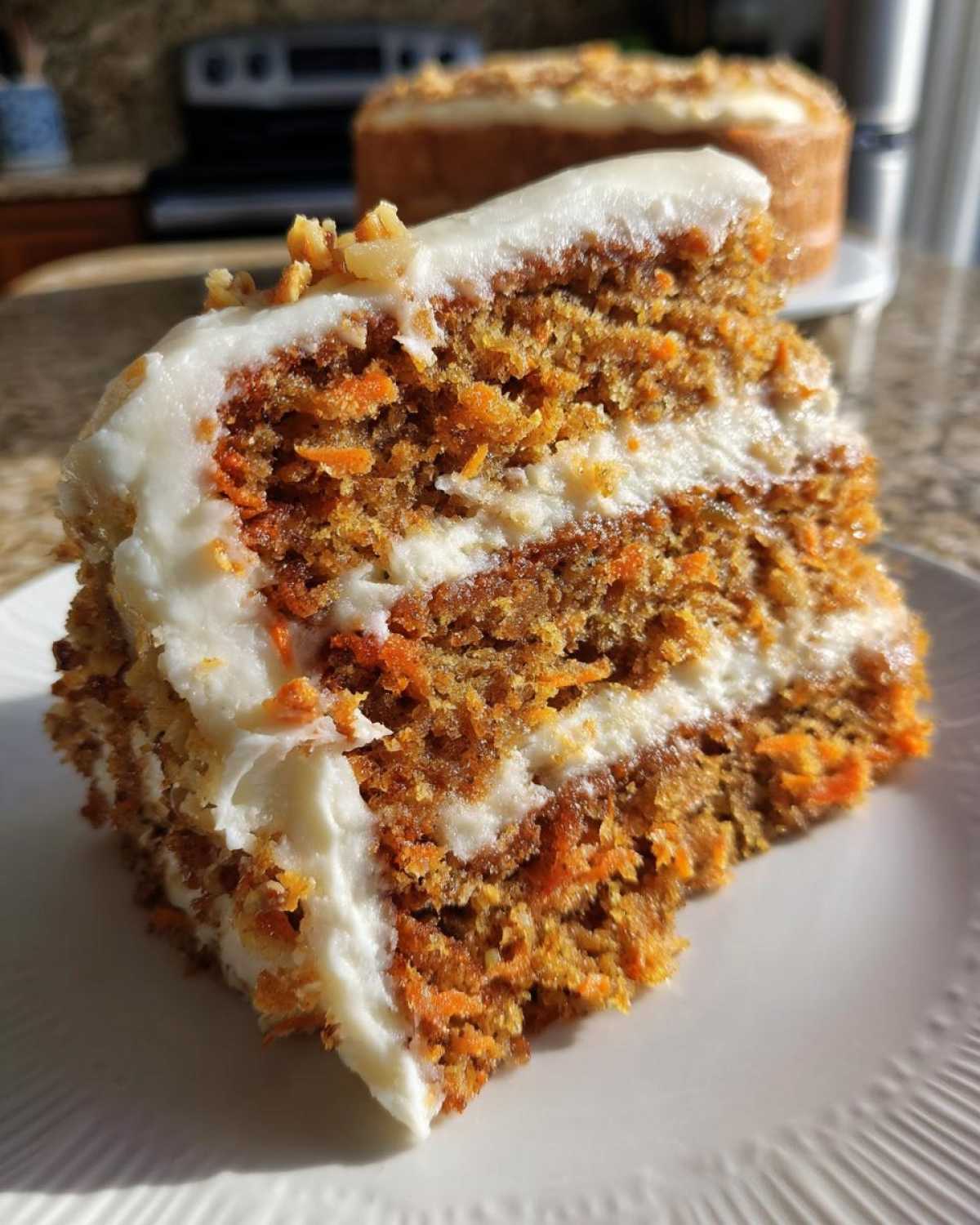 Close-up of a thick slice of carrot cake recipe showing layers of moist cake and cream cheese frosting, topped with walnuts.