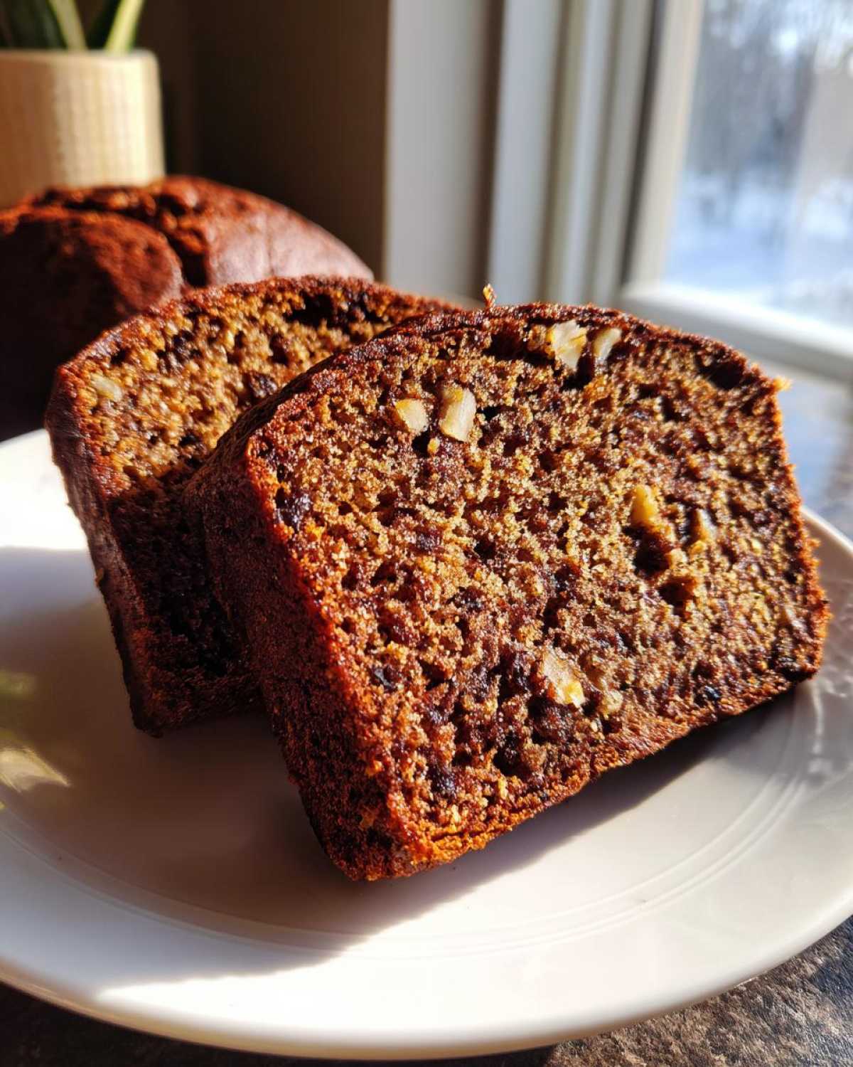 Two thick slices of moist date nut bread showing a rich brown crumb and visible pieces of walnuts.