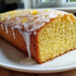 Close-up of a moist lemon pound cake loaf topped with white glaze and lemon zest.