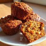 A stack of three moist morning glory muffins, with one cut open showing carrots and nuts inside.