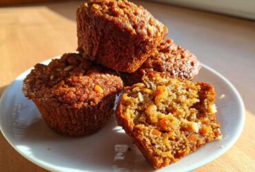 A stack of three moist morning glory muffins, with one cut open showing carrots and nuts inside.
