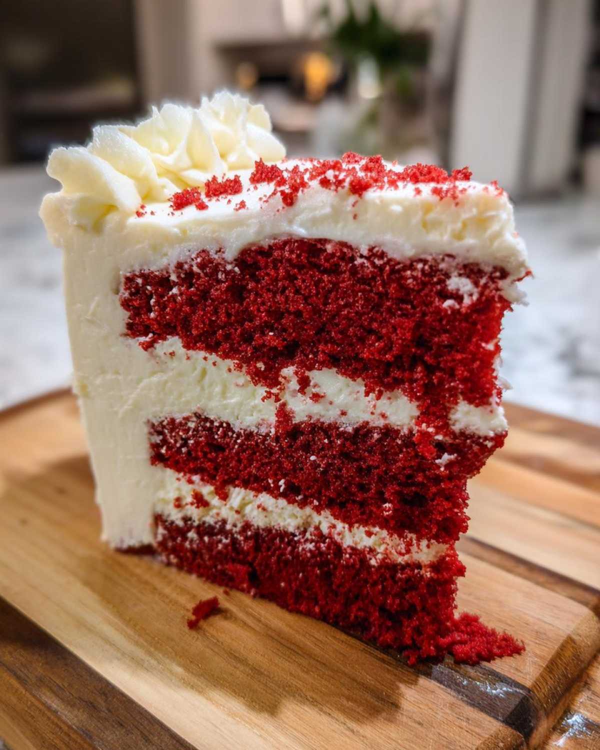 A tall, moist slice of red velvet cake showing three layers of deep red cake separated by white cream cheese frosting.