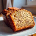 Close-up of a moist slice of sugar free banana bread showing nuts and dark specks in the crumb.