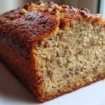 Close-up of a moist slice of sugar free banana bread loaf with a golden-brown crust and visible banana flecks.