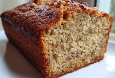 Close-up of a moist slice of sugar free banana bread loaf with a golden-brown crust and visible banana flecks.