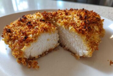 Close-up of a juicy parmesan crusted chicken breast cut in half, showing the white interior and golden crust.