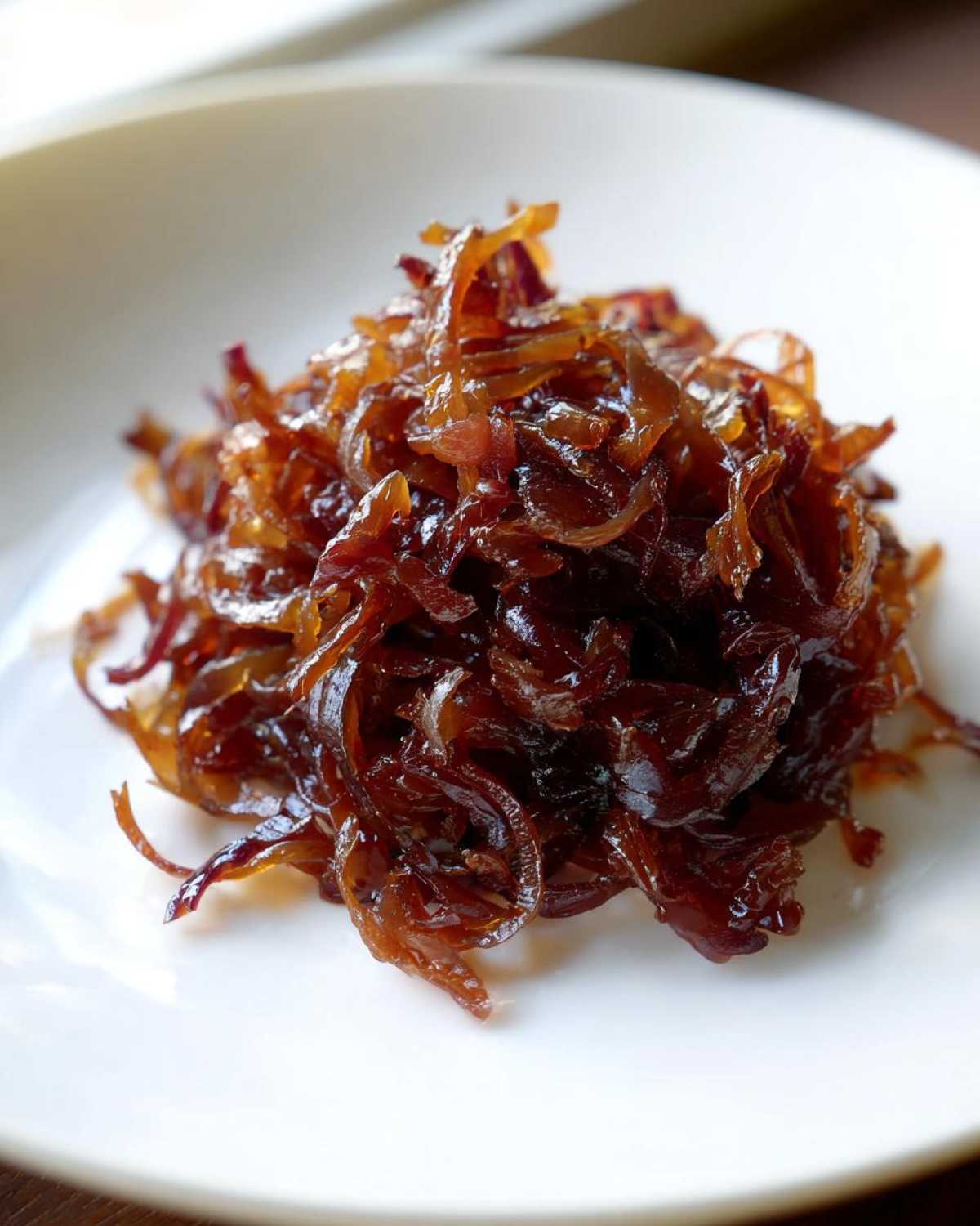Close-up of a mound of rich, dark brown caramelized onions served on a white dish.