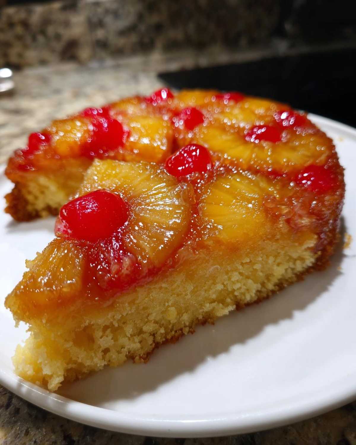 A moist slice of pineapple upside down cake topped with caramelized pineapple rings and maraschino cherries.