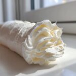 Close-up of a piping bag filled with fluffy vanilla buttercream frosting, showing a decorative swirl tip.
