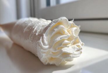 Close-up of a piping bag filled with fluffy vanilla buttercream frosting, showing a decorative swirl tip.