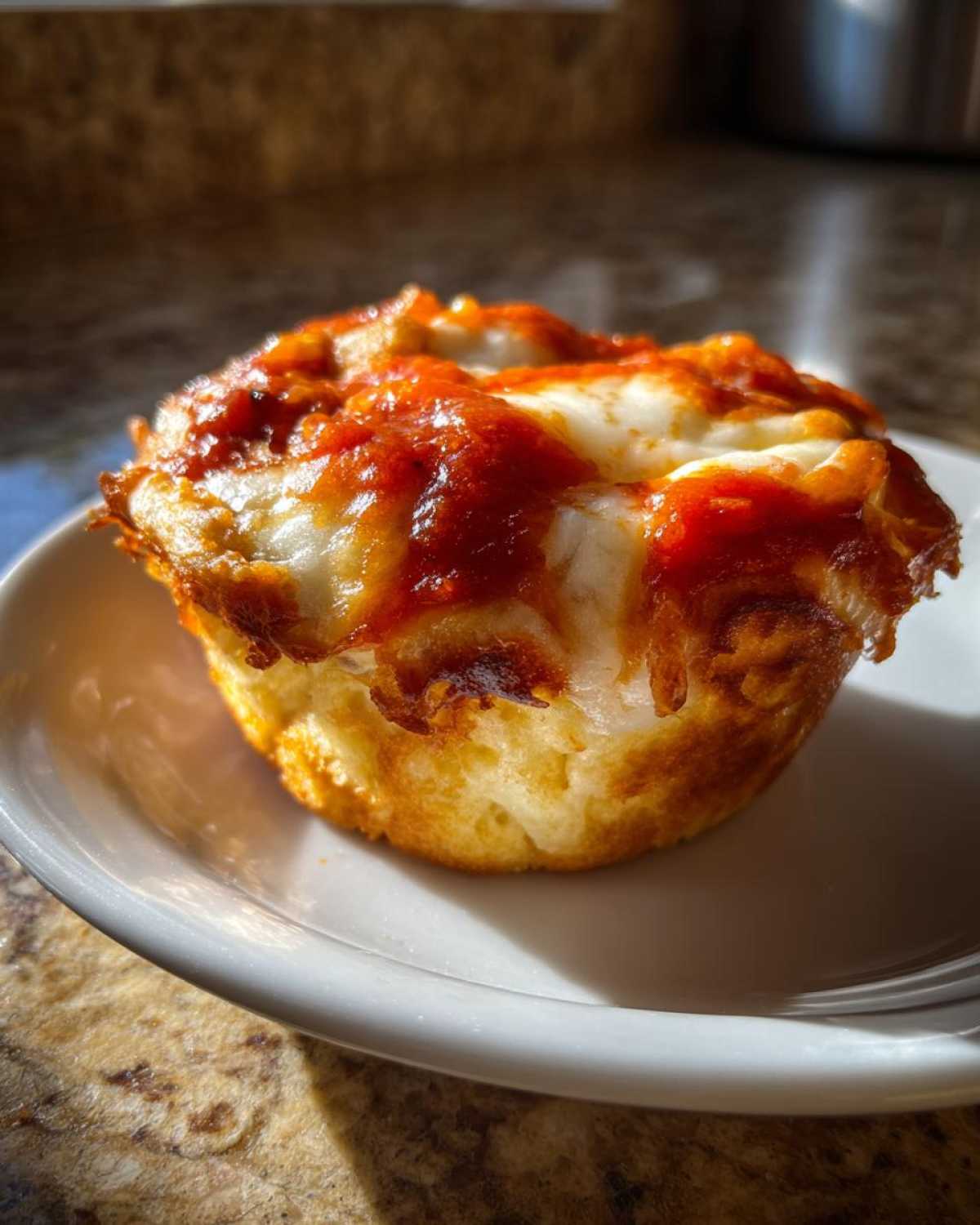 Close-up of a single, freshly baked pizza muffin with melted mozzarella cheese and tomato sauce on top.