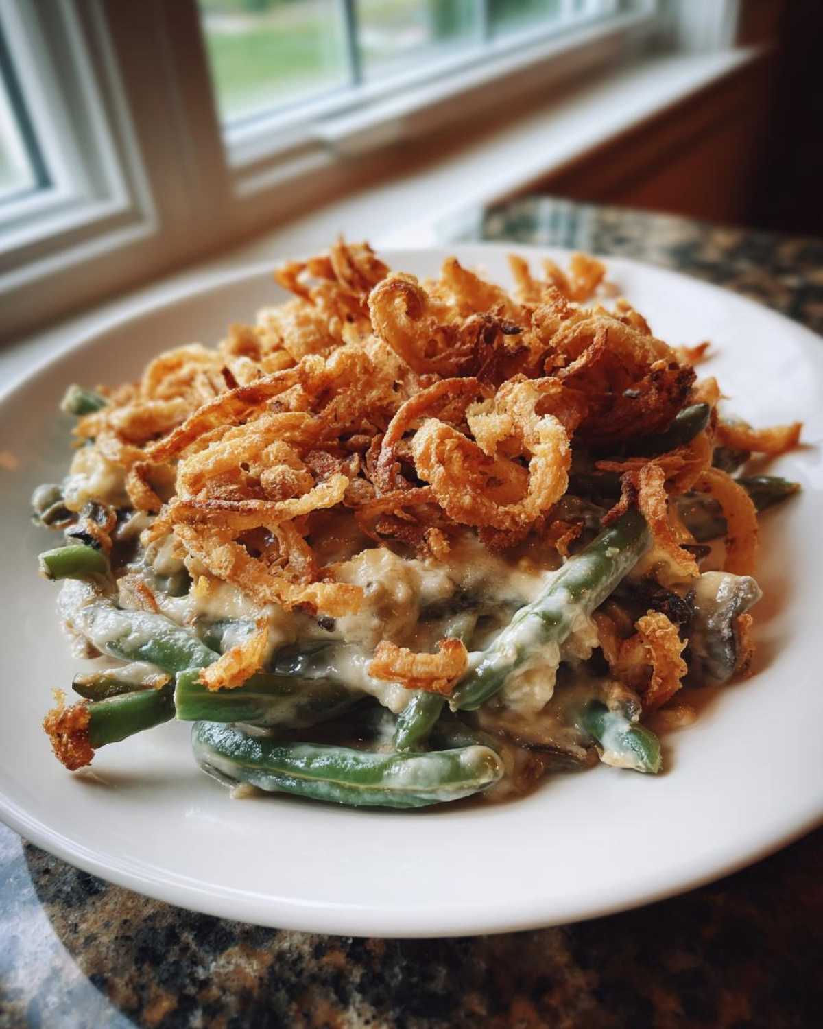 A close-up serving of creamy green bean casserole topped generously with crispy fried onions.