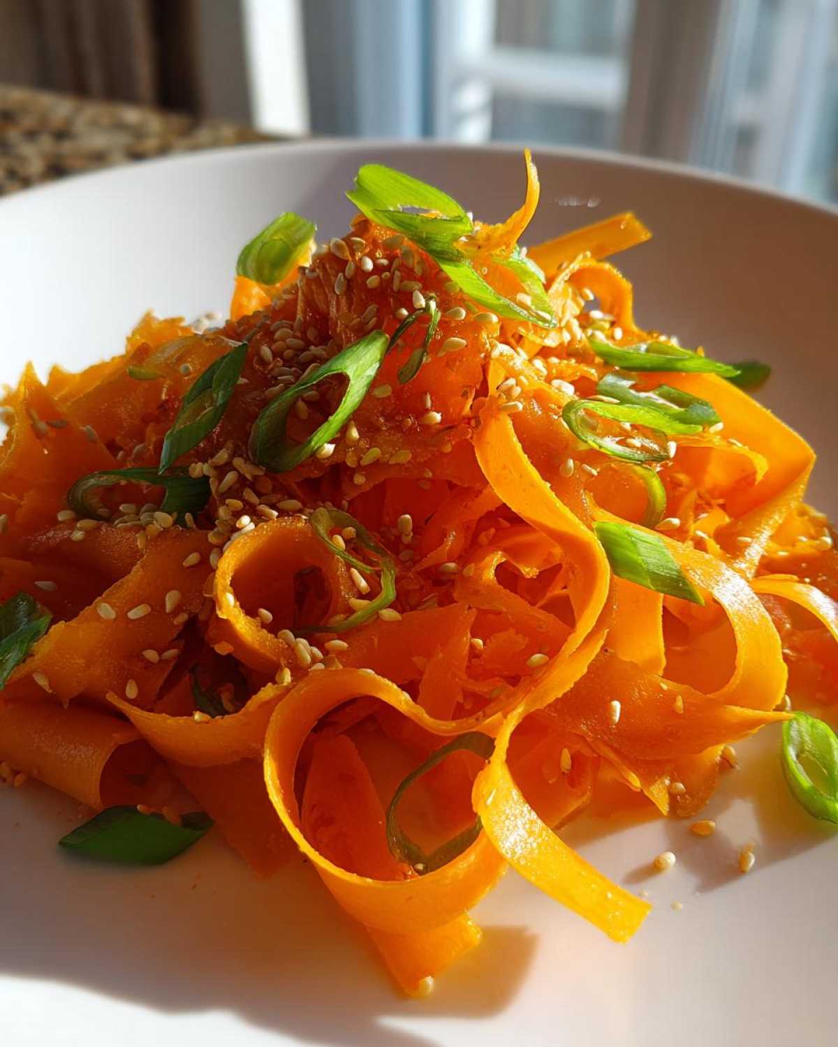 Close-up of a vibrant raw carrot salad featuring shaved carrot ribbons, sesame seeds, and sliced green onions.