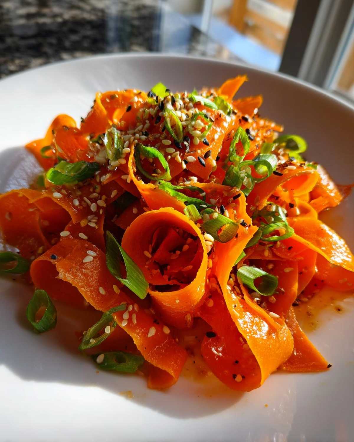 Close-up of a vibrant raw carrot salad featuring shaved carrot ribbons, sesame seeds, and sliced green onions.