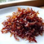Close-up of a small pile of deeply browned, rich caramelized onions on a white plate.