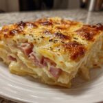 A thick, square slice of cheesy scalloped potatoes and ham with a golden-brown, bubbly top.