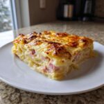 A thick, golden-brown slice of scalloped potatoes and ham baked in a creamy sauce, served on a white plate.