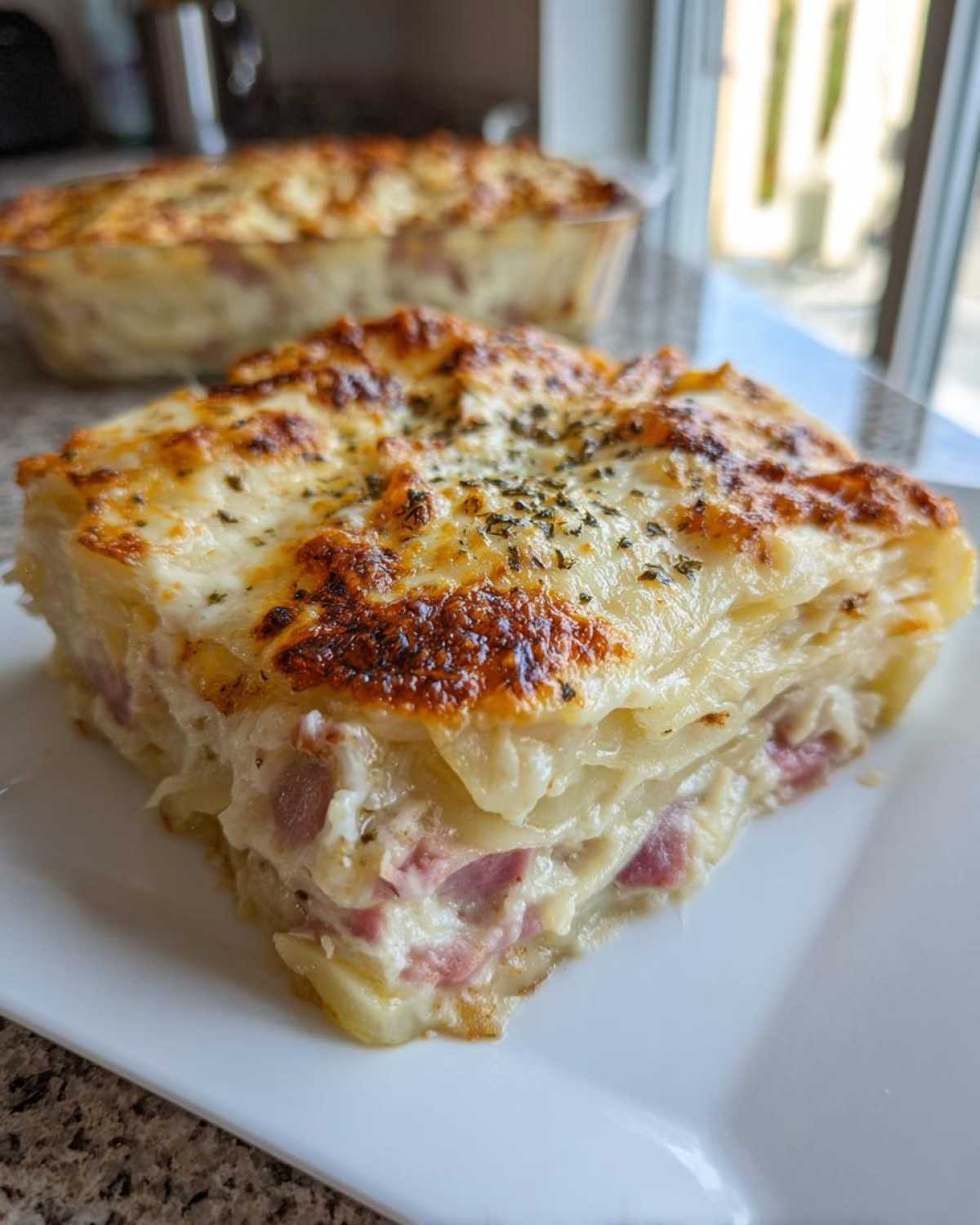 A square slice of creamy scalloped potatoes and ham layered casserole with a browned, cheesy top.