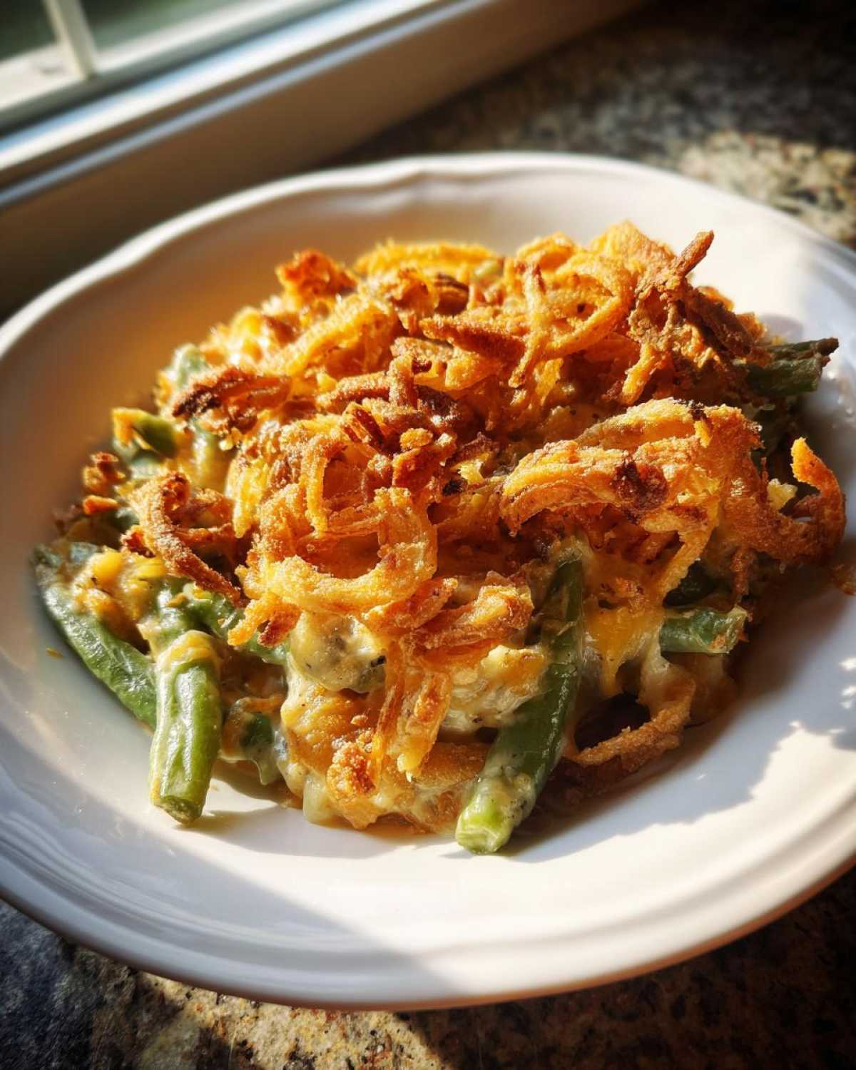 A close-up serving of creamy green bean casserole topped generously with crispy fried onions.
