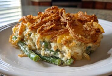 A close-up serving of creamy green bean casserole topped generously with golden, crispy fried onions.
