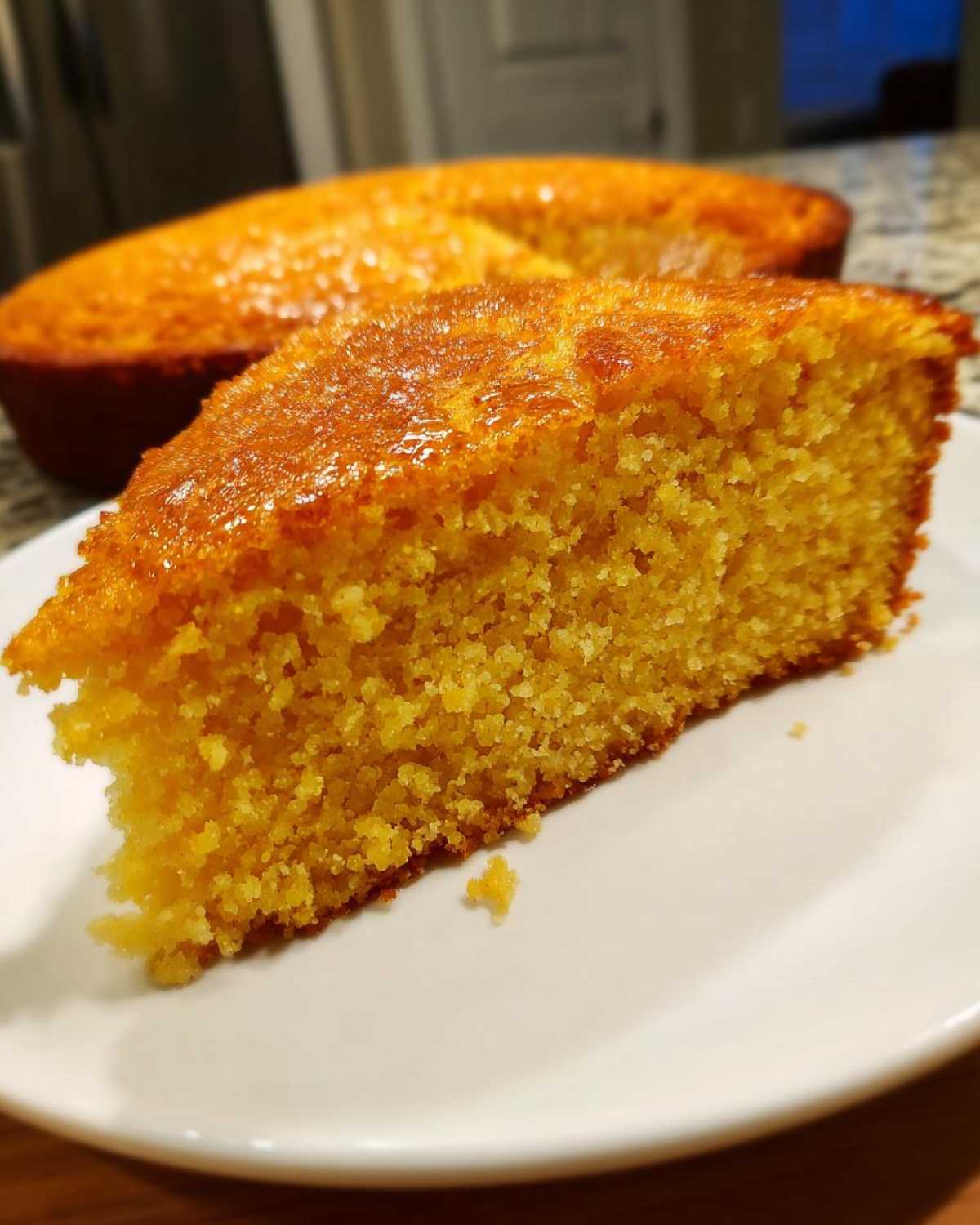 Close-up of a moist, golden slice of skillet cornbread drizzled with honey on a white plate.